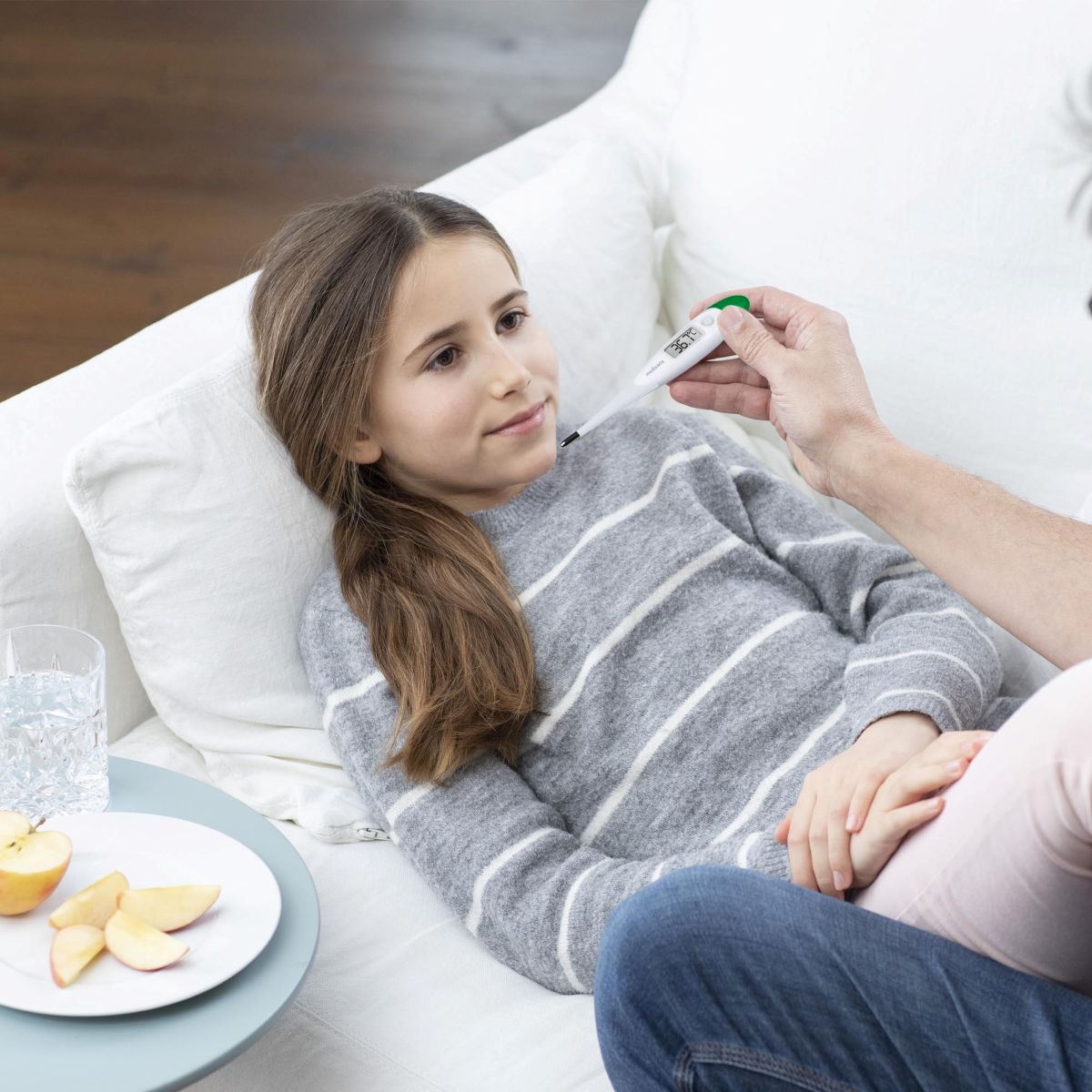 Kind liegt auf dem Sofa und ein Erwachsener misst die Temperatur mit einem medisana-Fieberthermometer.